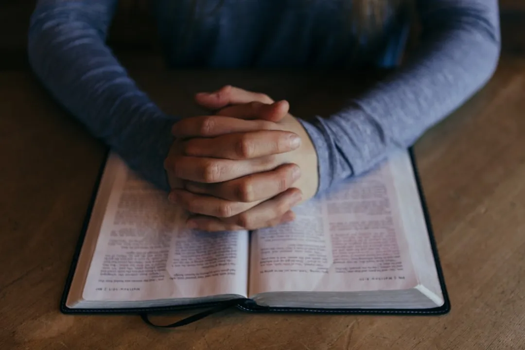 A man's hands resting on an open Bible on a table