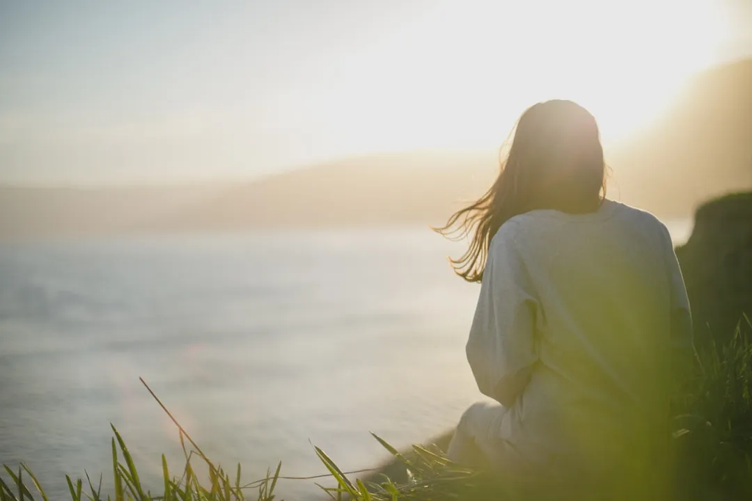 A woman standing and facing the sea in thoughtful reflection at sunset