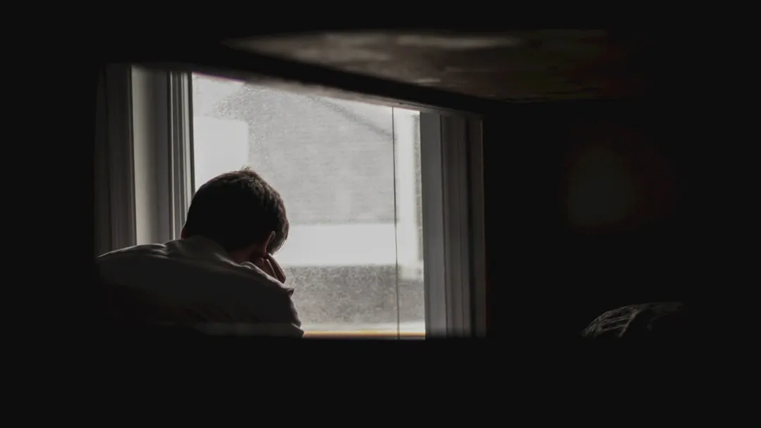 A person looking out a rain-streaked window in quiet thought