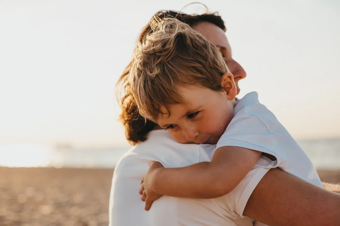 A young boy warmly hugging a woman outdoors during the day