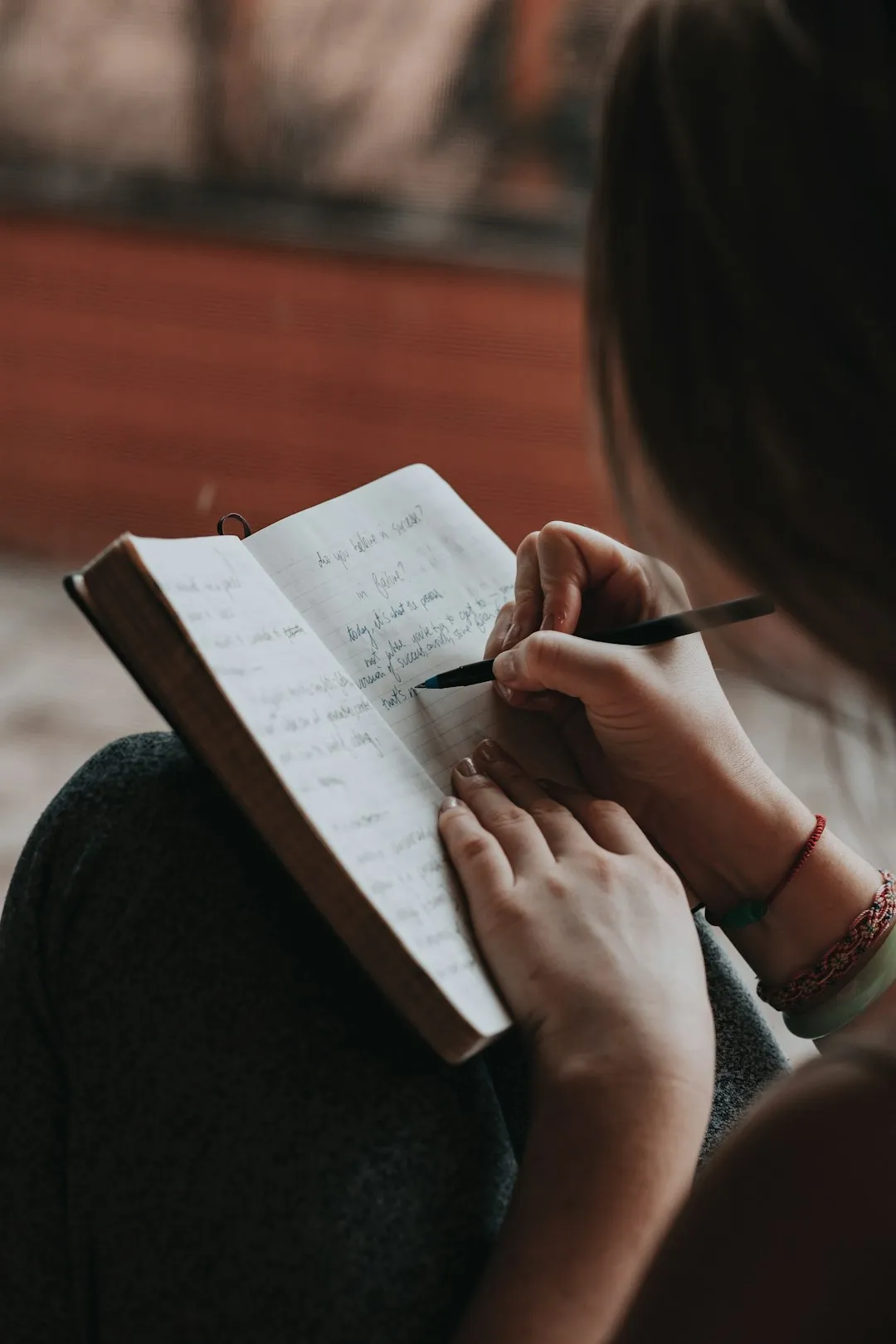 A woman writing thoughtfully in a notebook with a pen