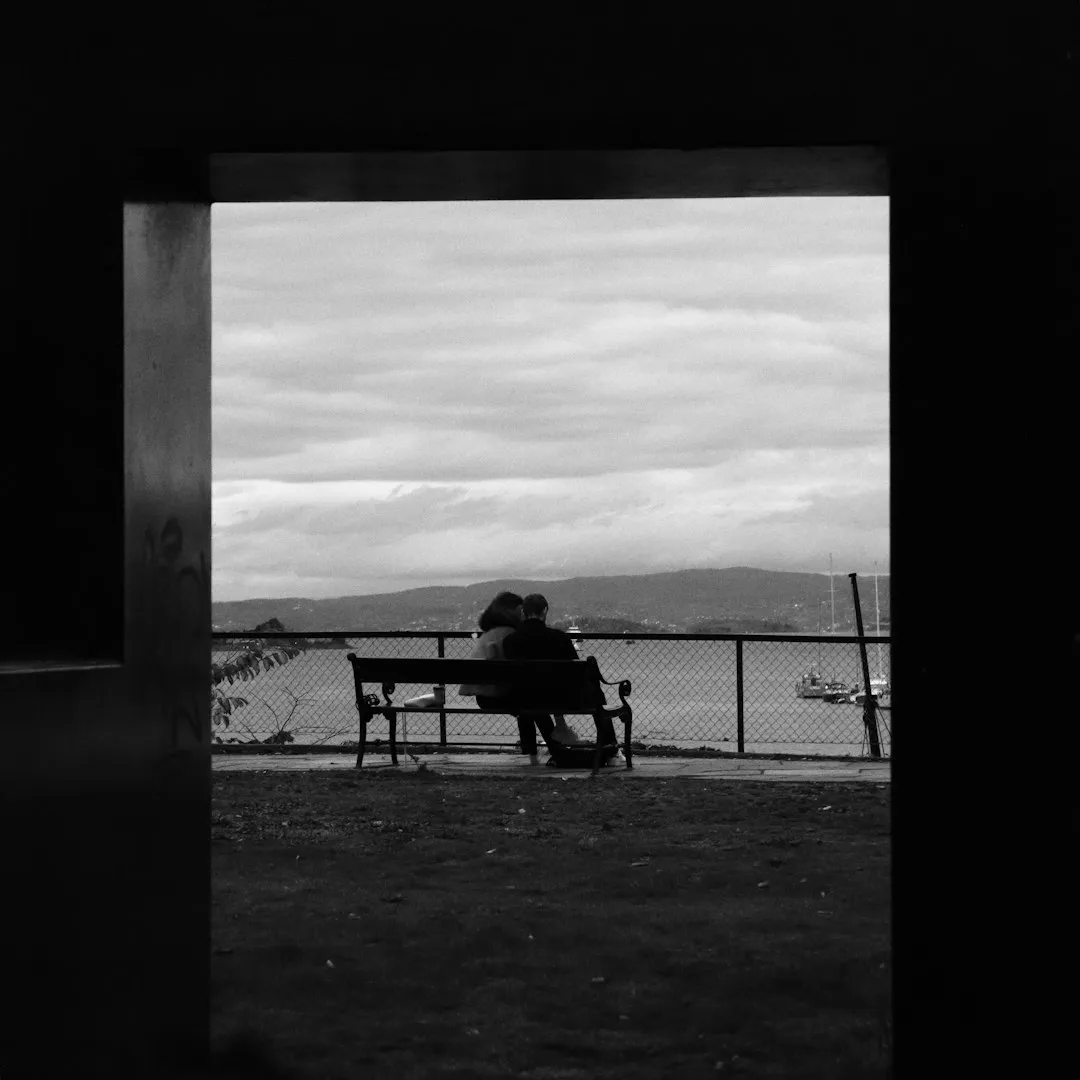 A grayscale photo of two people sitting quietly together on a bench
