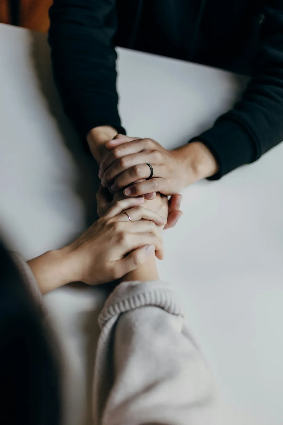 Two people sitting at a table, one comfortingly holding the other's hands in support