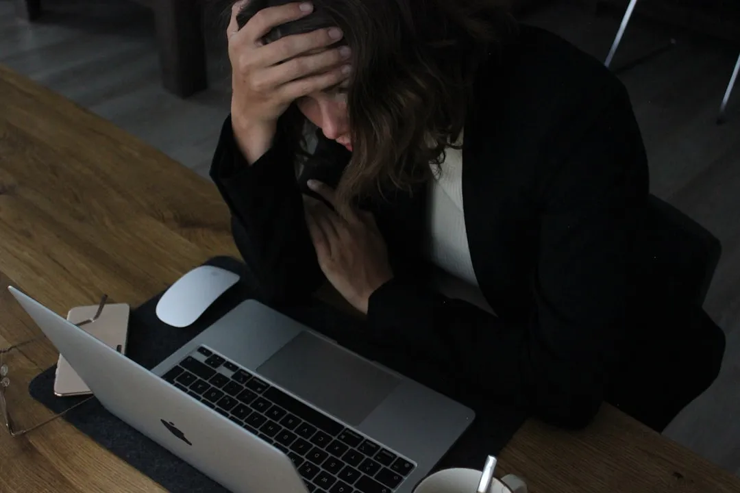 A stressed woman sitting at a laptop with her head resting in her hands